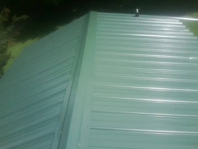 New green metal panels meeting at the ridge of a roof — Flat Roof Repair work by our crew in Madison